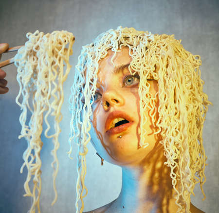 Funny hungry girl with curly noodles on her head.の写真素材