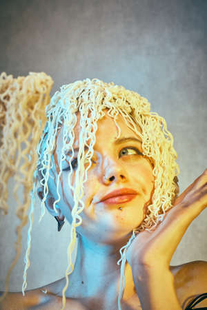 Funny hungry girl with curly noodles on her head.の写真素材