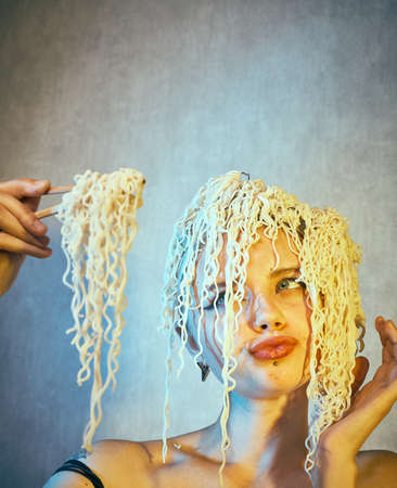 Funny hungry girl with curly noodles on her head.の写真素材