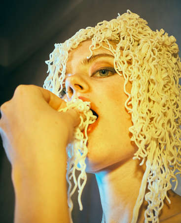 Funny hungry girl with curly noodles on her head.の写真素材