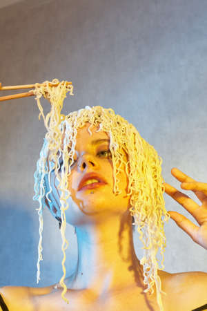Funny hungry girl with curly noodles on her head.の写真素材