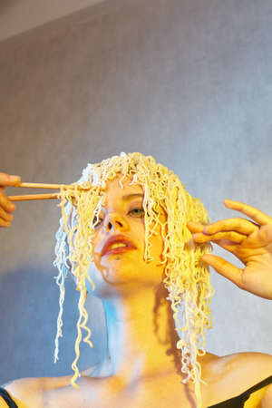 Funny hungry girl with curly noodles on her head.の写真素材