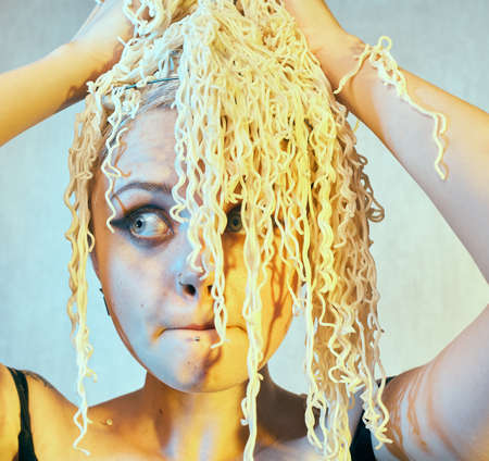 Funny hungry girl with curly noodles on her head.の写真素材