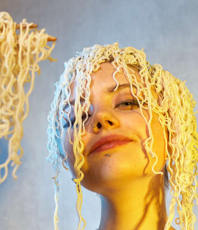 Funny hungry girl with curly noodles on her head.の写真素材