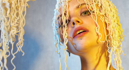 Funny hungry girl with curly noodles on her head.の写真素材