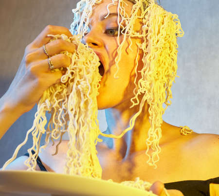 Funny hungry girl with curly noodles on her head.の写真素材