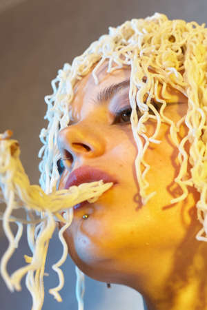 Funny hungry girl with curly noodles on her head.の写真素材