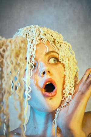 Funny hungry girl with curly noodles on her head.の写真素材