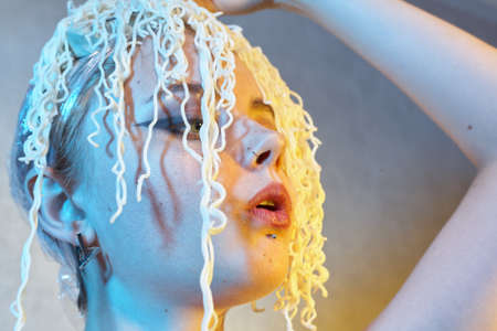 Funny hungry girl with curly noodles on her head.の写真素材