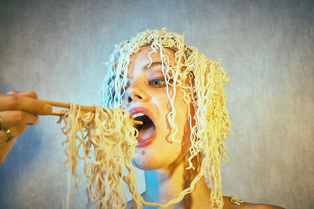 Funny hungry girl with curly noodles on her head.の写真素材