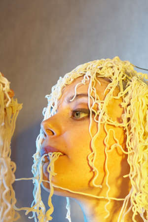 Funny hungry girl with curly noodles on her head.の写真素材