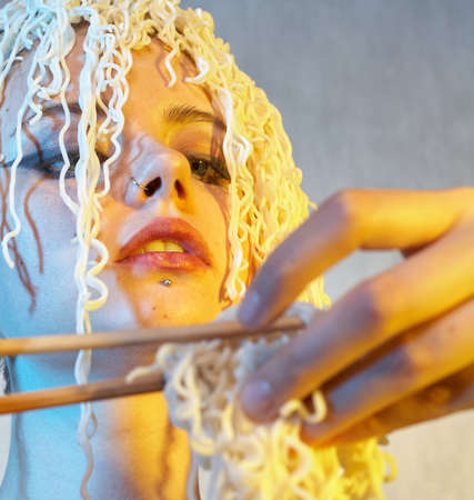 Funny hungry girl with curly noodles on her head.の写真素材