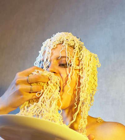 Funny hungry girl with curly noodles on her head.の写真素材