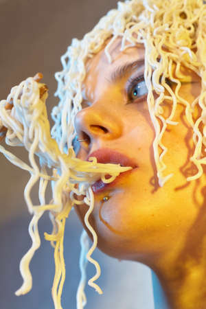 Funny hungry girl with curly noodles on her head.の写真素材