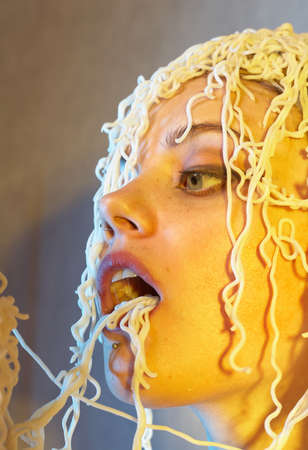 Funny hungry girl with curly noodles on her head.の写真素材