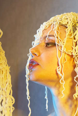 Funny hungry girl with curly noodles on her head.の写真素材