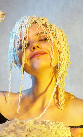 Funny hungry girl with curly noodles on her head.の写真素材