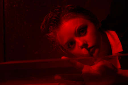 Horrible portrait of a young girl in a horror room with a red light.の写真素材