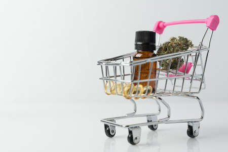 Supermarket trolley with marijuana bud and medical cannabis oil cbd on white background.の写真素材