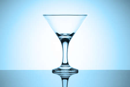 Empty martini glass stands on a glossy table with reflection. Cold blue tinted vignette.の写真素材