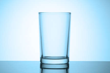 Empty simple glass for water stands on a glossy table with reflection. Cold blue tinted vignette.の写真素材