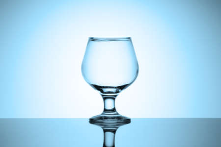 Empty cognac glass stands on a glossy table with reflection. Cold blue tinted vignette.の写真素材