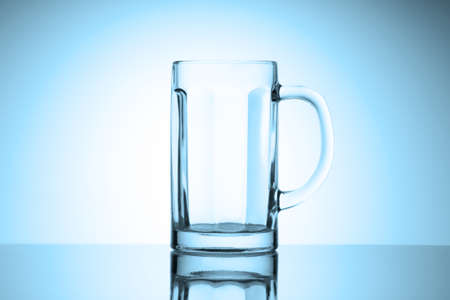 Empty beer mug glass stands on a glossy table with reflection. Cold blue tinted vignette.の写真素材