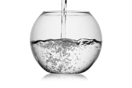 Splash jet of water pours in glass fishbowl with bubbles isolated on a white background without glare. Reflection on the surface. Back light.の写真素材