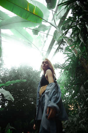Beautiful young blonde girl portrait outdoors in a botanical garden among exotic plants.