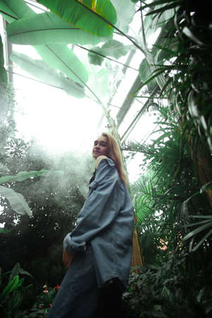 Beautiful young blonde girl portrait outdoors in a botanical garden among exotic plants.の写真素材