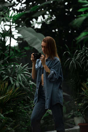 Beautiful young tourist girl with a camera in a botanical garden photography plants and nature.の写真素材