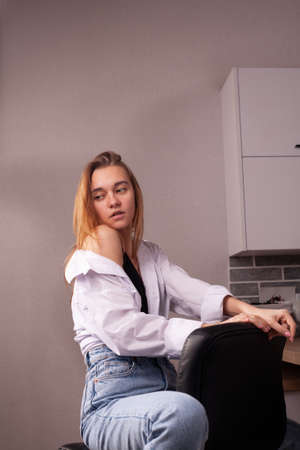 Portrait of a beautiful blonde girl in simple everyday things sitting indoors.の写真素材