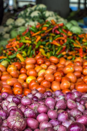 Pile of onions next to a pile of tomatoes and peppers on a marketの写真素材