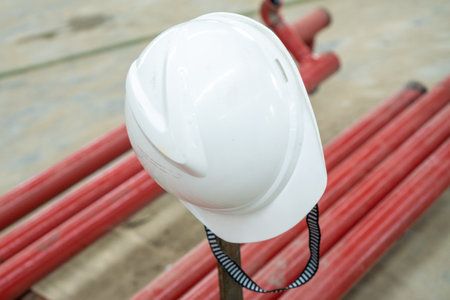 White plastic hard hats for safety equipment and Occupational Health and Safety (OHS) fittings. Located above a metal pipe painted red which is in a development project.の写真素材