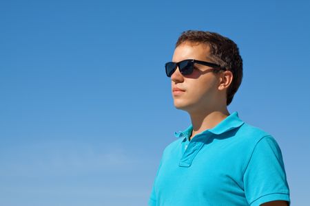 young serious man in sunglasses against blue skyの写真素材