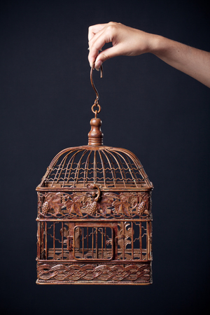 vintage birdcage in female hand isolated on dark backgroundの写真素材