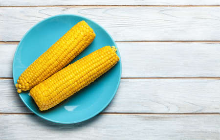 boiled corn on blue plate on white wooden backgroundの写真素材