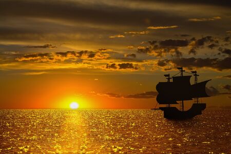 seascape with a golden setting sun and the silhouette of a sailboatの写真素材