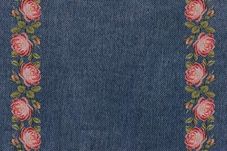 frame of embroidered pink roses on a blue denim background close upの写真素材
