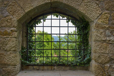 grated window in an old stone wall with a landscape in the background. close-upの写真素材