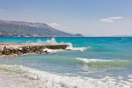 The shore of the blue sea with big waves and mountains in the backgroundの写真素材