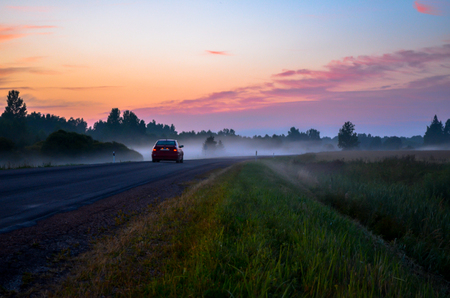 Car driving into the forest fog at sunsetの写真素材