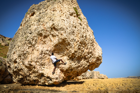 "Give me a challenge and I'll meet it with joy." A man climbs a rock on rocky and rugged terrainの写真素材