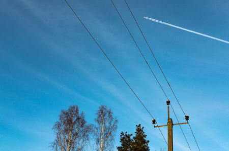 A plane in high flight above tree tops and telephone linesの写真素材