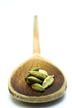 Green cardamom pods in a wooden spoon on a white background.の写真素材