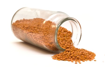 Red lentils spilling out of a glass jar on a white backgroundの写真素材