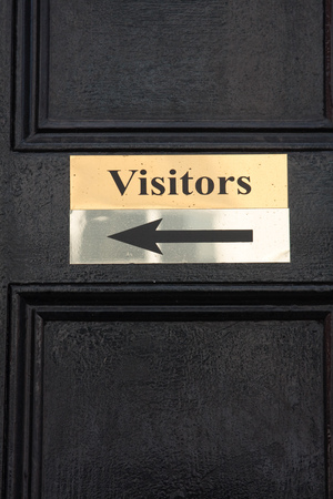 A brass directional visitors  sign on a black doorの写真素材