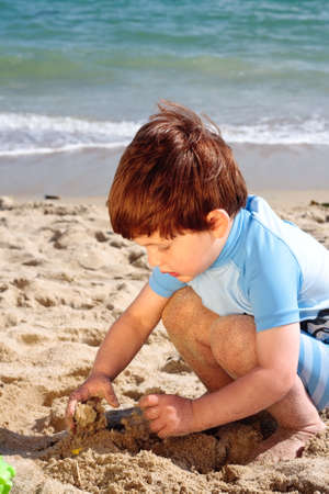 A young 3 year old boy playing with the sand on a beachのeditorial素材