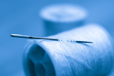 A blue toned close-up image of a needle and cotton reels
