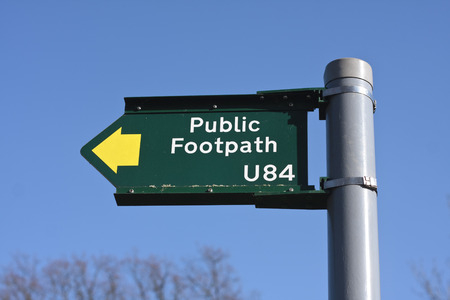 A green public footpath sign against a blue sky